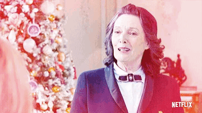 a woman wearing a tuxedo and bow tie is standing in front of a christmas tree with a netflix logo behind her