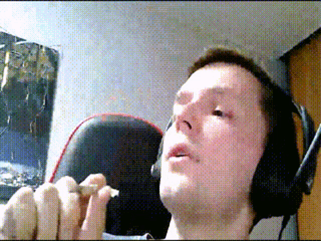 a man wearing headphones is smoking a cigarette in front of a poster