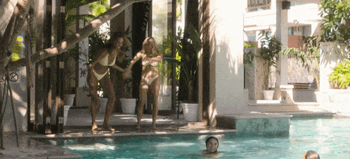 two women in bikinis are standing next to a pool with a no smoking sign