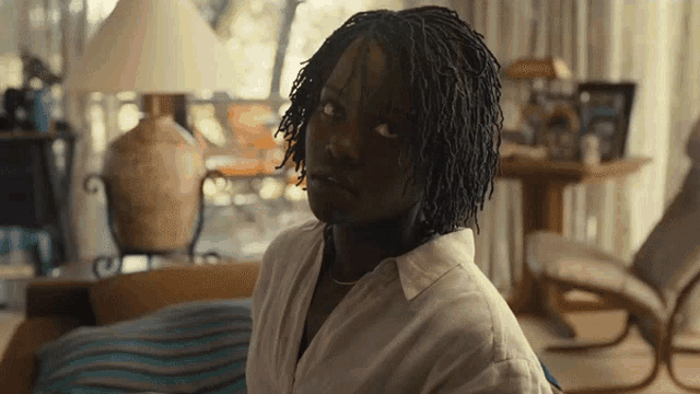 a woman with dreadlocks is sitting on a couch and looking at the camera
