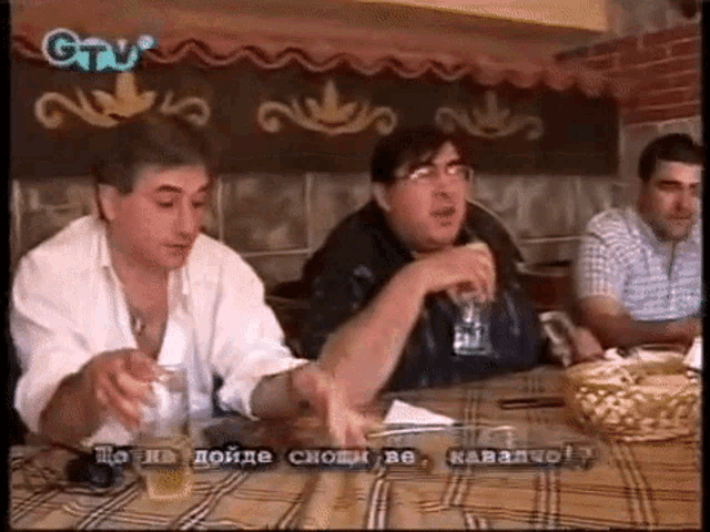 a group of men are sitting at a table drinking beer and smoking cigarettes .