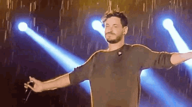 a man with a beard is standing on a stage with his arms outstretched and holding a microphone .