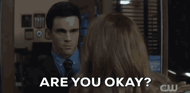 a man in a suit and tie is talking to a woman in a room and asking her if she is okay .