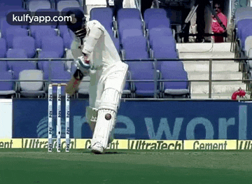 a cricket player is playing a game of cricket on a field with a sign in the background that says ultratech cement .