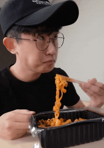 a young man wearing glasses and a hat that says nothing on it is eating noodles with chopsticks