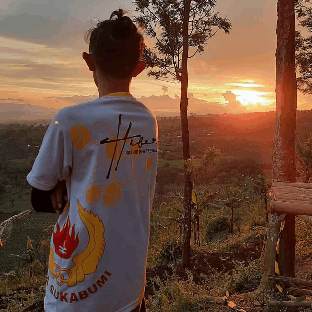 a person wearing a shirt that says sukabumi looks at the sunset
