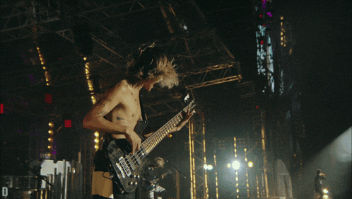a shirtless man is playing a guitar on stage