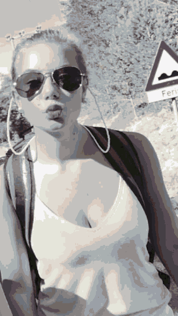 a woman wearing sunglasses is blowing a kiss in front of a sign that says feri