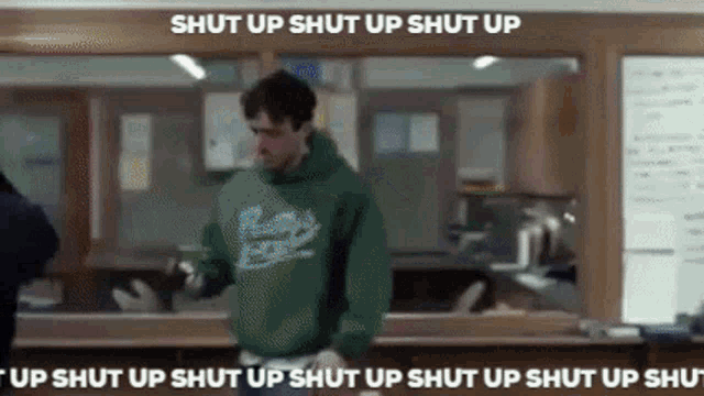 a man in a green hoodie is standing in front of a window with the words shut up shut up shut up