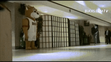 a mascot wearing a bucks jersey is standing in a hallway ..
