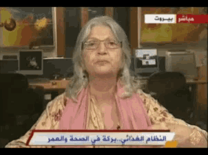 a woman with glasses and a pink scarf is on a tv screen with arabic writing