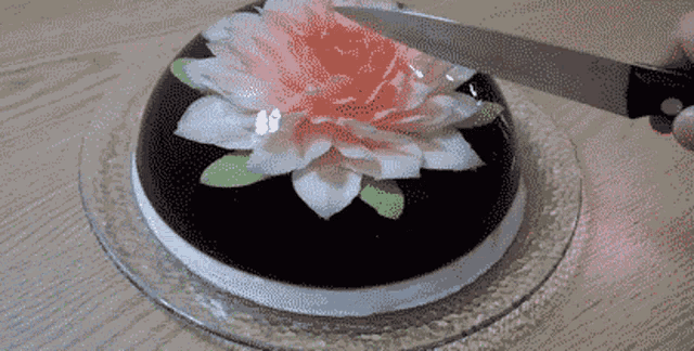 a person is cutting a cake with a pink flower on it