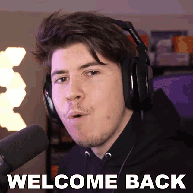 a man wearing headphones is standing in front of a microphone and says welcome back