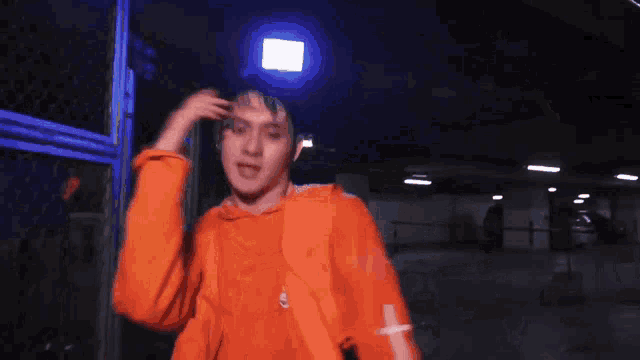 a man in an orange hoodie is standing in front of a blue light