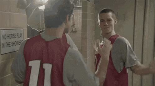 two young men are standing in a locker room talking to each other .