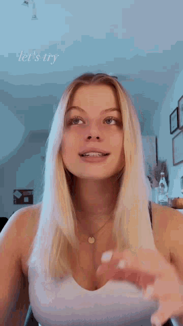 a woman in a white tank top is holding her hair in her hands and making a funny face .