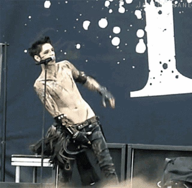a shirtless man singing into a microphone in front of a large letter l