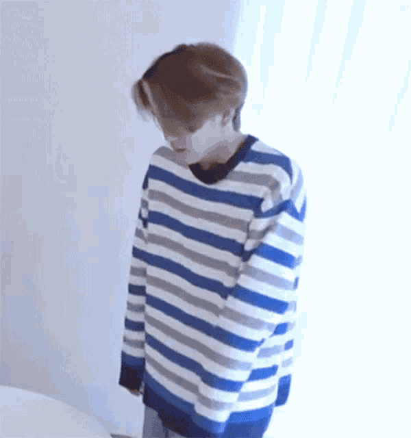 a man wearing a blue and white striped sweater is standing next to a window .