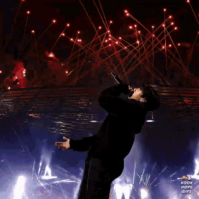 a man is singing into a microphone on a stage with fireworks behind him .