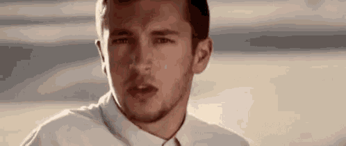 a man with a beard is wearing a white shirt and tie and looking at the camera .