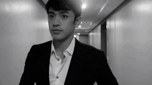 a black and white photo of a man in a suit walking down a hallway .