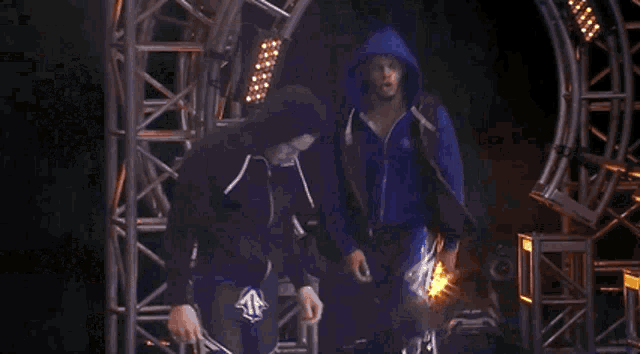 a man in a blue hoodie is standing in front of a spotlight .