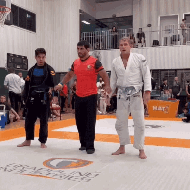 three men are standing on a mat that says mat 1