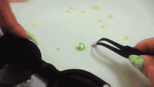 a person with green nails is holding a pair of tweezers over a green bead .