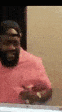 a man wearing a pink shirt and a black hat is standing in front of a mirror
