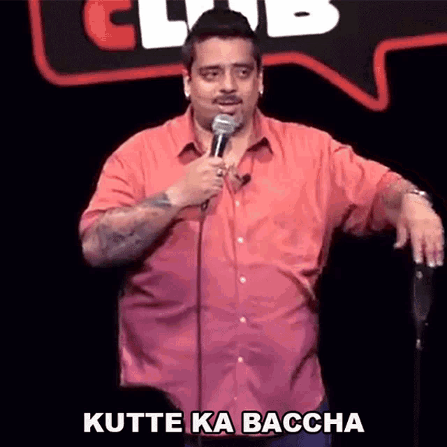 a man in a red shirt is standing in front of a microphone and saying kutte ka baccha