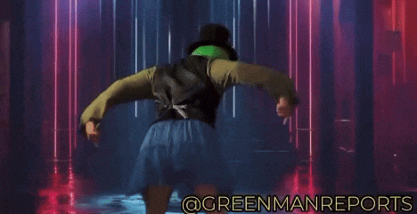 a woman in a skirt and top hat is dancing in a dark room with the words @greenmanreports below her
