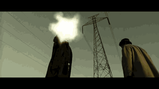 a man in a trench coat is standing in front of a power line