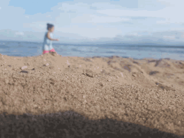 a little girl is standing on a sandy beach