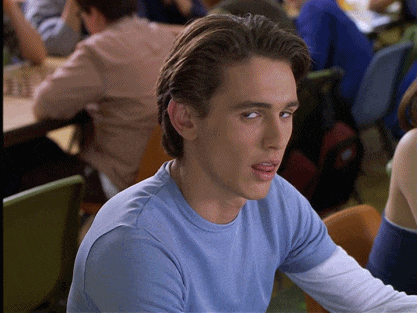 a young man wearing a blue shirt is sitting in a classroom