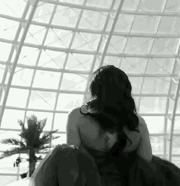 a woman without a shirt is sitting in front of a large window in a black and white photo .