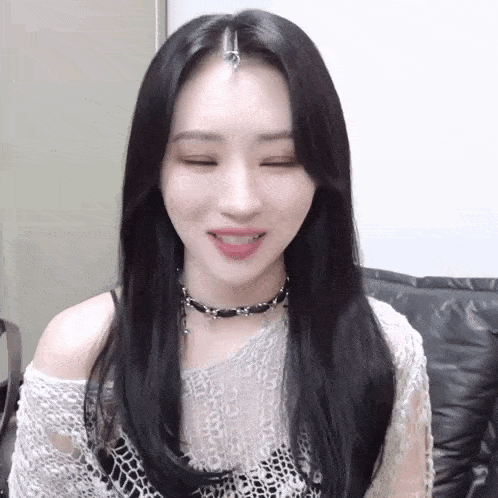 a woman with long black hair is smiling with her eyes closed and wearing a choker .