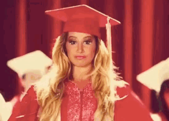 a woman in a red graduation cap and gown is standing in front of a red curtain .