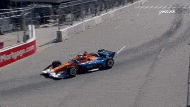 a race car is driving down a track with a peacock logo in the background