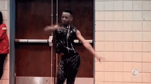 a man in a black sequined dress is dancing in front of a door .
