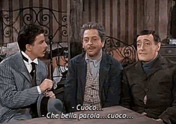 three men are sitting at a table talking to each other and one of them is saying cuoco che bella parola cuoco .