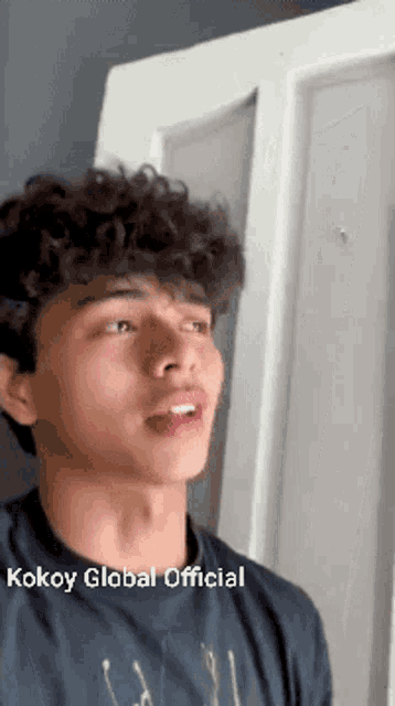 a young man with curly hair is wearing a kokoy global official shirt .