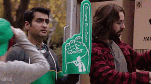 two men are standing next to each other holding a green foam hand .
