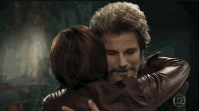 a man with a beard and a woman in a leather jacket are hugging each other