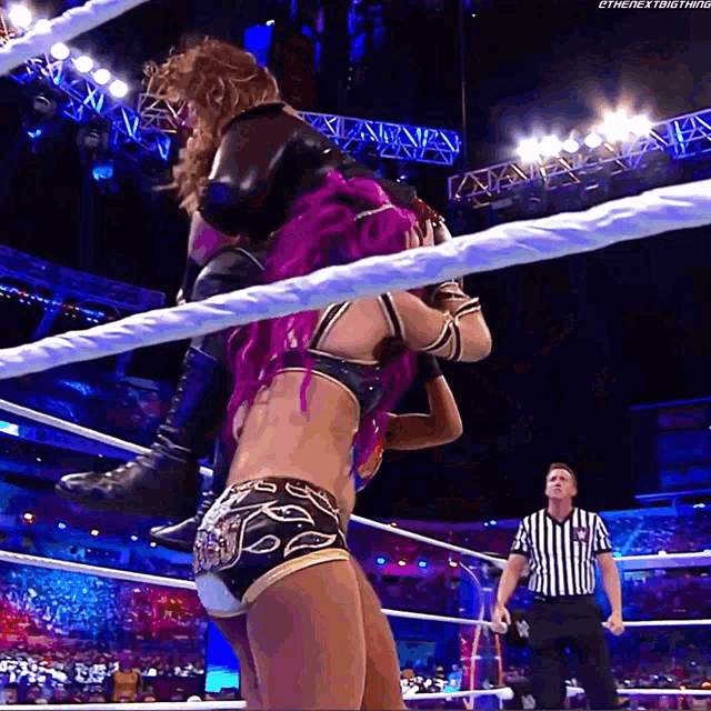 a female wrestler with purple hair is being lifted by another wrestler in a wrestling ring