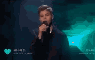 a young man is singing into a microphone on a stage in front of a crowd .