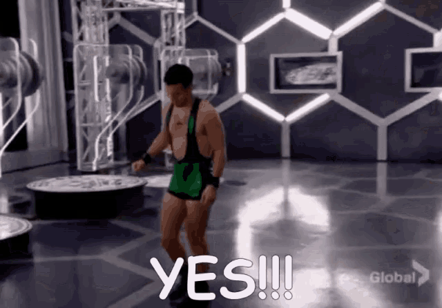 a man in a green wrestling outfit is dancing in a room with the words yes written on the floor
