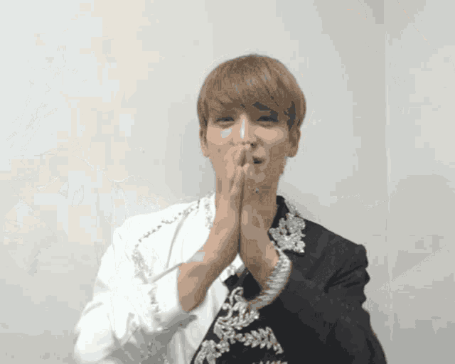 a man covering his mouth with his hands in front of a white wall