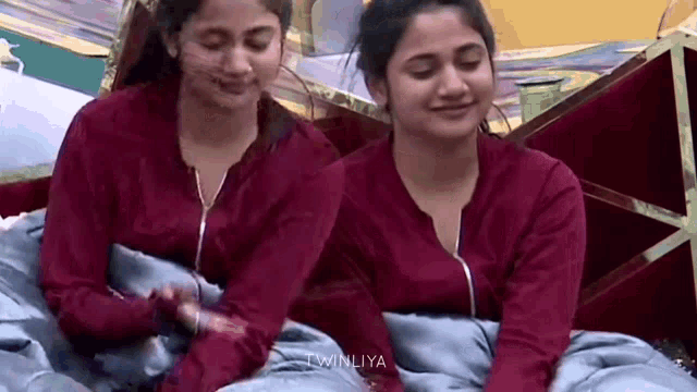 two women in red shirts are sitting next to each other in a bed .