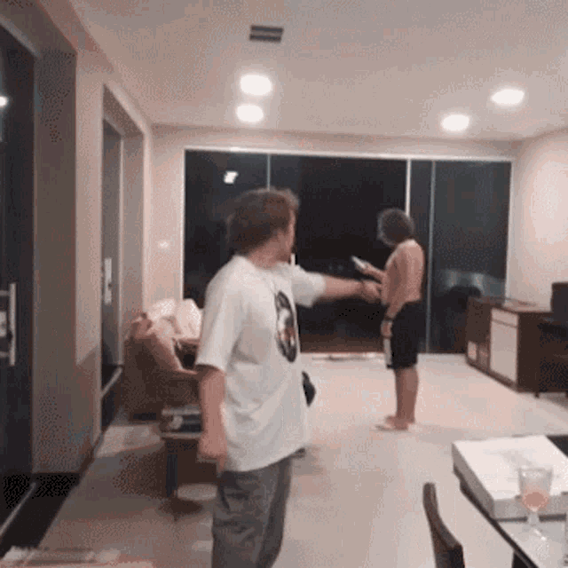 a man in a white shirt is standing in a living room with a woman looking at her phone