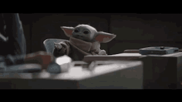 a baby yoda toy is sitting at a table with a person .